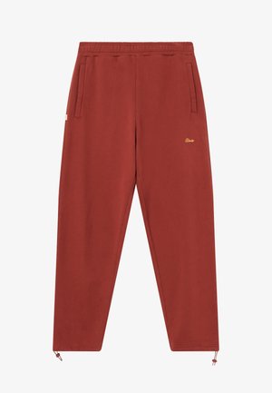 Punased dressipüksid, millel on nööriga tupe, kaks külgmist taskut ja kuldne logo tikand vasaku tasku lähedal. Pehme kangas sujuva tekstuuriga.