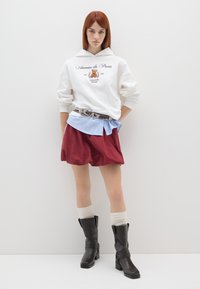 Witte hoodie met "Avenue de Paris" print, rode shorts, gelaagd lichtblauw shirt, bloemenriem, kniehoge zwarte laarzen en crèmekleurige sokken.