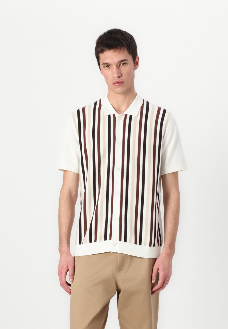 Bela kratka srajca s kratkimi rokavi, okrašena z navpičnimi črtami v rjavi, bež in temno rdeči barvi. Gladka tekstura s klasičnim ovratnikom.