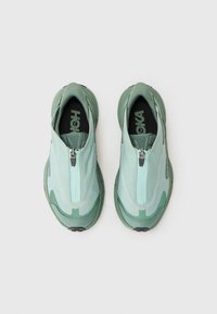 Baskets slip-on vert clair avec une fermeture éclair, tige synthétique texturée, col rembourré et logo noir contrastant sur la semelle intérieure.