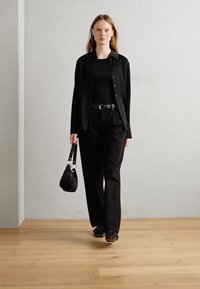 Ensemble noir comprenant un haut ajusté, un pantalon ample et une chemise à boutons. Les accessoires incluent une ceinture noire et un petit sac à main. Textures lisses.