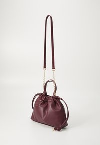Sac à main en cuir bordeaux avec un haut froncé, deux poignées et une bandoulière en chaîne amovible. Texture lisse et éclat subtil. Accents en métal doré.