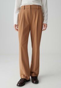 Bruine op maat gemaakte broek met een hoge taille, geplooide voorkant en wijduitlopende pijpen. Gemaakt van een gladde stof, met een nette afwerking en riemlussen.