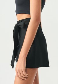 Svarta högmidjade shorts tillverkade av ett slätt tyg, med en framknutningsdetalj och utsvängd design.