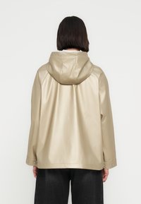 Χακί ελαφρύ μπουφάν με κουκούλα και λεία, γυαλιστερή υφή. Διαθέτει κουμπιά τύπου σναπ στα μανίκια και χαλαρή σιλουέτα.