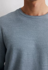 Jasnoniebieski sweter z teksturowanym splotem, z klasycznym okrągłym dekoltem. Materiał ma lekki stretch i jednolity, równy wzór przez całą powierzchnię.