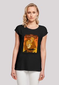 Svart kortermet t-skjorte med et fargerikt Lion King-preg som viser Simba og Mufasa på en bakgrunn i oransje og gult.