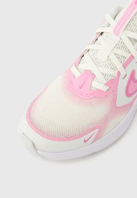 Λευκό και ροζ αθλητικό παπούτσι με πλέγμα στο πάνω μέρος, υφασμένα διακοσμητικά στοιχεία, στρογγυλεμένη μύτη και λογότυπο. Διαθέτει κορδόνια και επενδεδυμένη σόλα.