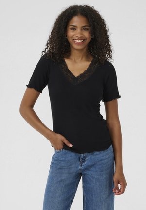 Black short-sleeve top with a V-neck and lace trim. Features a ribbed texture and scalloped sleeves, paired with blue denim jeans.