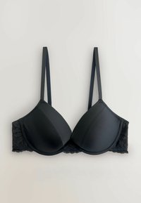 Čierna podšitá podprsenka s nastaviteľnými tenkými ramienkami a čipkovým zdobením pozdĺž pásu, položená na neutrálnej podkladovej ploche.