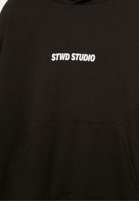 Sweatshirt noir avec une poche avant et un texte imprimé blanc "STWD STUDIO" centré sur la poitrine.