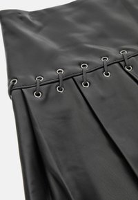 Juoda klostuota odinė sijonas su metalinėmis akytėmis ir šnerysčių detale juosmens srityje, išsiskiriantis lygiu paviršiumi ir struktūrine forma.