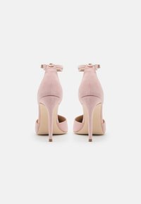 Růžové semišové lodičky s špičatou špičkou, tenkým jehlovým podpatkem a řemínkem kolem kotníku ozdobeným kulatou metalickou přezkou.