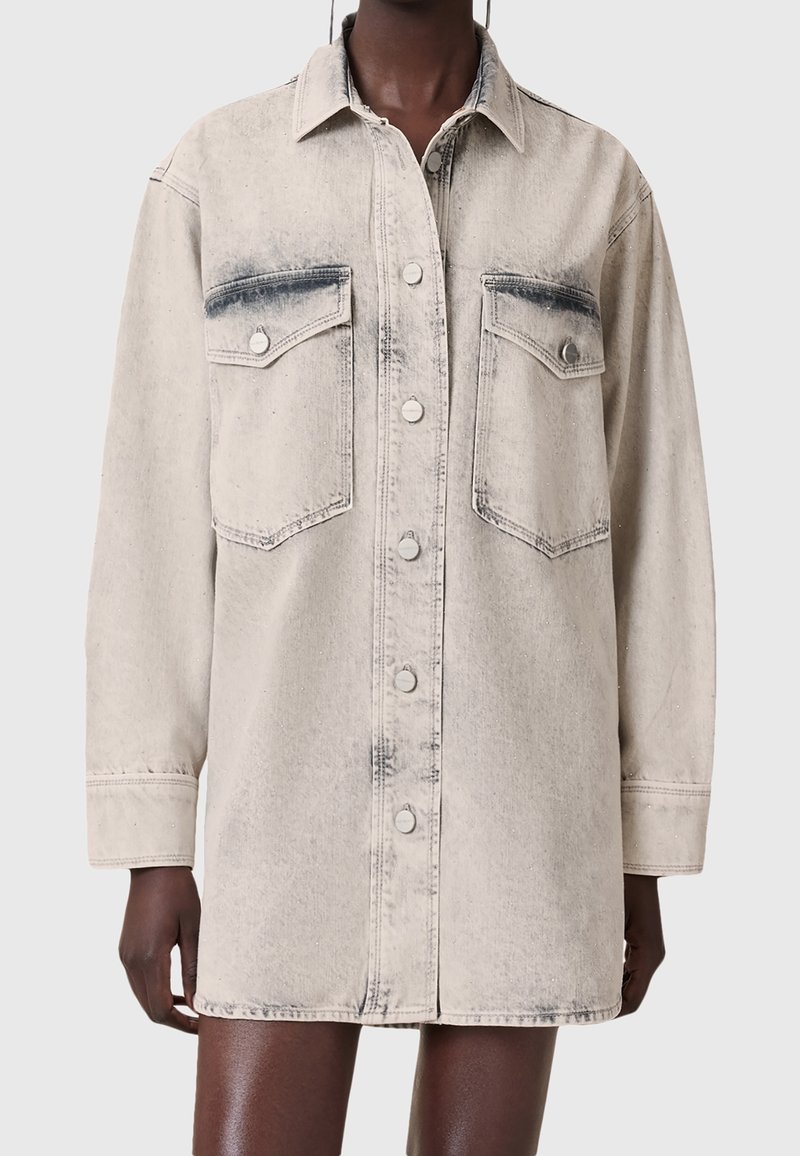 Veste en denim léger lavé à manches longues avec fermeture boutonnée sur le devant et deux poches poitrine à rabat portée par une personne.