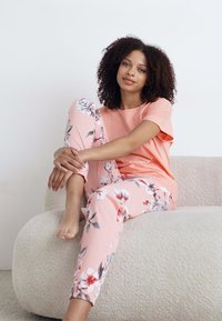Ljusrosa bomulls-T-shirt kombinerad med blommönstrade rosa pyjamasbyxor. Tyget har en mjuk textur och har löv och blommor i vitt och grönt.