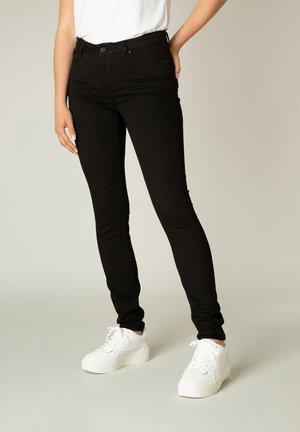 Black skinny jeans made of denim with a smooth texture; features five pockets and a classic button-fly closure, paired with white platform sneakers.