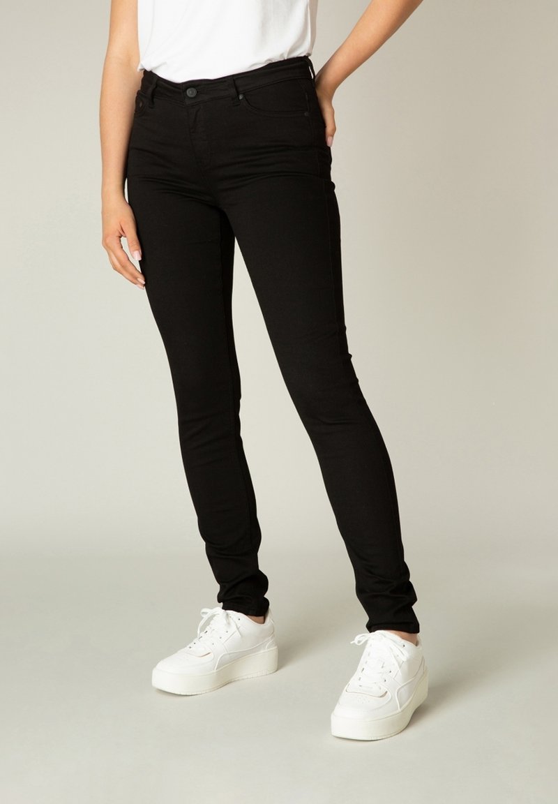 Zwarte skinny jeans van denim met een soepele textuur; voorzien van vijf zakken en een klassieke knoopsluiting, gecombineerd met witte platform sneakers.