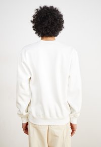 Sweatshirt blanc à col rond avec des poignets et un ourlet côtelés, texture douce et coupe décontractée. Vu de l'arrière, sans marque ni motifs visibles.