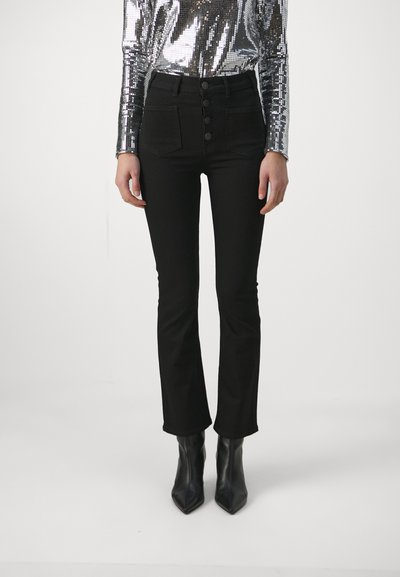 Jean évasé noir à taille haute, avec un devant à boutons, deux poches avant et un matériau en coton lisse. Associé à des bottes noires à bout pointu.