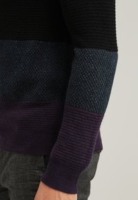 Sweter wykonany na drutach w poziome paski w kolorach czarnym, niebieskim i fioletowym; teksturowany materiał, ściągacze oraz dopasowany fason. Miękki, warstwowy wygląd.