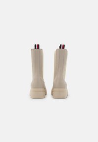 Botas de tobillo crema hechas de cuero suave con una suela gruesa, con costuras verticales y una pestaña de tiro multicolor en la parte posterior.