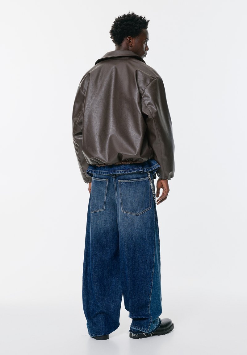 Hnedá umelá kožená bunda s voľným strihom a zníženými plecami, skombinovaná s oversized modrými džínsami s na Gathered pásom a reťazovým detailom.