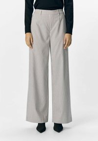 Weit geschnittene Hose im gestreiften Muster mit hoher Taille, aus leichtem Stoff in einer neutralen Farbpalette, kombiniert mit schwarzen Absätzen.