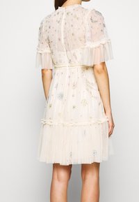 Beige tüllklänning med korta puffärmar, broderade blommönster och stjärnmönster i olika färger, rynkad midja, lager av volangmudd.