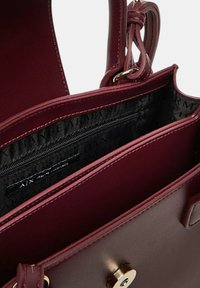 Borsa color bordeaux con esterno in pelle liscia, dotata di chiusura con zip superiore, tasca interna con zip e dettagli in metallo dorato.