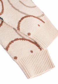 Neulepaita vaaleassa beessissä, jossa on ruskeita pyöreitä kuvioita ja pieniä pisteitä. Ribbausteet hihansuissa ja pehmeä rakenne lisäävät mukavuutta ja istuvuutta.