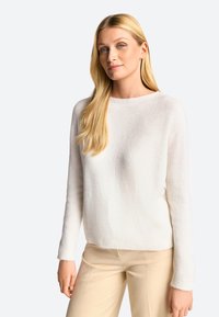 Vit stickad tröja med rund hals, ribbade ärmslut och nederkant. Mjuk struktur, avslappnad passform, kombinerad med ljusbeige byxor.