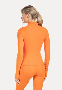 Orange träningsöverdel med långa ärmar i stretchigt material, med en hög krage och figurnära design, lämplig för aktivt bruk.