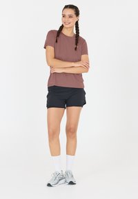 Kortärmad, mauve atletisk tröja tillsammans med svarta shorts, bärs med vita strumpor och ljusgrå löparskor. Enkelt design och passform.