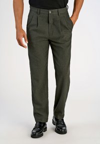 Zielone dopasowane spodnie z teksturowanej tkaniny, w kant, z zapięciem na guzik i kieszeniami bocznymi, w połączeniu z czarnymi, wypolerowanymi butami.