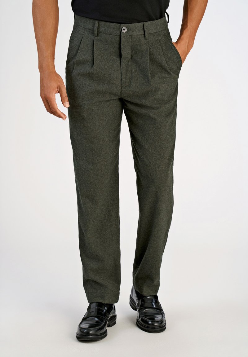 Zielone dopasowane spodnie z teksturowanej tkaniny, w kant, z zapięciem na guzik i kieszeniami bocznymi, w połączeniu z czarnymi, wypolerowanymi butami.