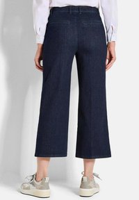 Culottes en denim noir à jambe large, dotées de poches et de passants de ceinture, associées à des baskets de couleur claire avec des détails en dentelle.