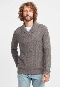 Grau gestrickter Pullover mit Schalkragen, der ein strukturiertes Muster und gerippte Bündchen aufweist. Getragen mit hellblauen Jeans.