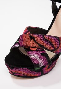 Sandale plateforme noire avec brides croisées brodées de motifs floraux rose vif, orange et violet.