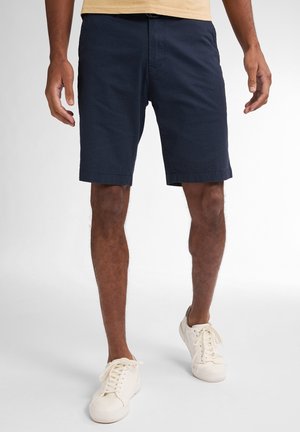 Marineblaue Shorts aus strukturiertem Stoff, mit geradem Schnitt, seitlichen Taschen und Knopfverschluss, kombiniert mit weißen Sneakers.