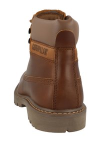 Bota de tobillo de cuero marrón con un panel textil color canela, costuras visibles, logo y suela texturizada. Diseñada para la durabilidad y el soporte.