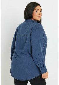 Camicia di denim blu scuro, con colletto, polsini con bottoni e una vestibilità rilassata con pieghe sul retro per maggiore libertà di movimento.