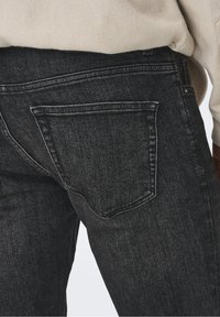 Jeans de denim gris oscuro con una textura ligeramente desgastada, que presentan bolsillos traseros con detalles de costura y un sutil efecto de decoloración.