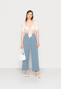 Blusa curta com estampa floral e mangas bufantes, com laços à frente. Calças de perna larga de cintura alta em azul claro. Bolsa branca e sandálias de salto.