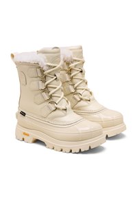 Beige vedenpitävät saappaat, joissa on keinoturkista vuorattu sisus, nauhakiinnitys, kullanväriset yksityiskohdat ja teksturoitu kumipohja, jossa on Vibram-logot.