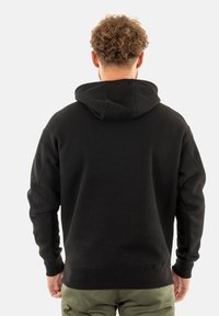 Felpa nera con cappuccio in tessuto texturizzato, polsini e vita a costine. Dotata di tasca a marsupio e vestibilità rilassata.