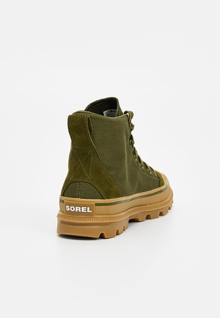 Grüner Stoff-Hochschaftschuh mit strukturierter Oberfläche, Gummisohle, runder Zehe und auffälligem weißen Logo an der Ferse. Die Schnürsenkel reichen bis nach oben.