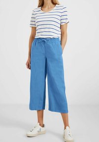 Wit en blauw gestreepte kortebloushemd gecombineerd met blauwe wijde broek en witte sneakers, met een elastische tailleband en een losse pasvorm.