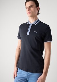 Mornarska polo majica z ožjim svetlo modrim ovratnikom, tremi gumbi in logotipom "BOSS" na prsih. Iz bombažnega materiala z gladko teksturo.