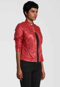 Rote Lederjacke mit gestepptem Muster auf den Schultern, hohem Kragen, Reißverschluss vorne und zwei vorderen Reißverschlusstaschen. Schlanker Schnitt.