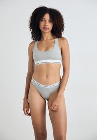 Sivi pamučni sport bra i thong set s širokim elastičnim pojasom s "Calvin Klein" logotipom. Glatka tekstura i dizajn s okruglim izrezom.